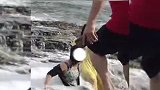 两名女子坐在海中礁石上拍照，被海浪拍落水中