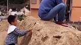 男子坐在沙堆打电话，殊不知儿子在背后挖沙玩