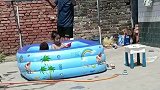 孩子在院里玩水，爷爷拿毯子垫铺在晾衣架上遮阳