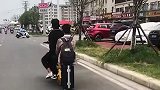 男子坐在行李箱上，好友则控制电单车前行