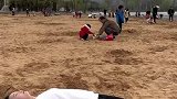 女子半身陷入沙地，现场表演跳舞，旁边的孩子看傻了