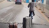 男子骑行共享单车，拖拽着两个行李箱前行
