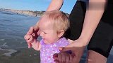 妈妈带宝宝到海边玩，一个海浪冲过来，宝宝的反应太可爱了