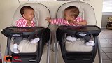 双胞胎萌娃坐在婴儿车里，看着对方开心地笑着，真是可爱啊！