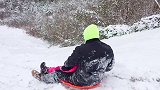 爸爸带着宝宝在雪地上滑行，从高坡往下滑，后面还有推手！