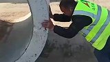 工人艰难推着圆管前行，男子在一旁加油助威