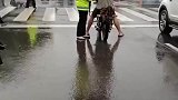 骑车人没穿雨衣，等红灯的时候，交警顺手撑起伞为他遮挡风雨