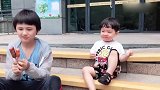 两个混血儿宝宝蹲在路边吃肠，哥哥喂弟弟画面太温馨了