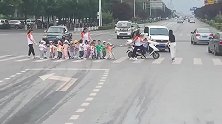 小朋友被老师牵着过马路，三位老师前后跟随着，路过的汽车没有一个催促！