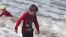 大浪冲了过来，小男孩躲闪不及，最终被大浪给冲翻了！