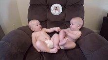 肉嘟嘟双胞胎坐沙发上，望着彼此牵手互撩啃脚丫，玩的不亦乐乎