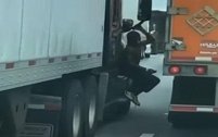 美国：一男子坐在卡车驾驶室外，在高速公路车流中搭便车