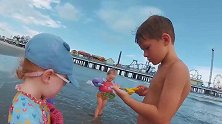 五胞胎穿着救生衣在海边玩，用水桶装海水的举动太可爱了